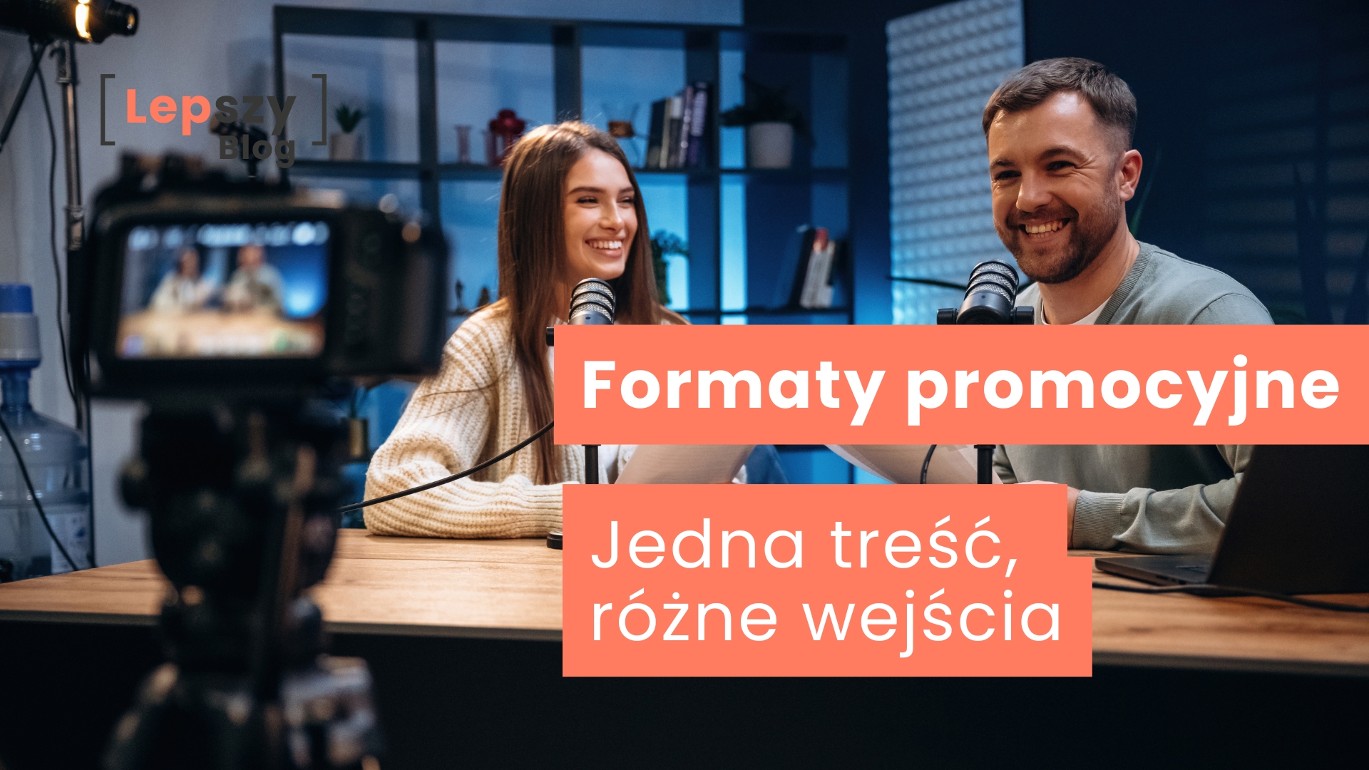 Dwie osoby siedzące przy stole i rozmawiające do mikrofonów, nagrywane przez aparat widoczny na pierwszym planie – napis „Formaty promocyjne. Jedna treść, różne wejścia”, symbol wielokanałowego opowiadania tej samej historii w różnych formach.
