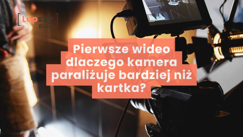 Na pierwszym planie wyraźna kamera skierowana w stronę osoby stojącej w tle, która jest lekko rozmyta; na obrazie widnieje napis „Pierwsze wideo. Dlaczego kamera paraliżuje bardziej niż kartka?”, symbolizujący napięcie i tremę towarzyszącą pierwszym nagraniom wideo.