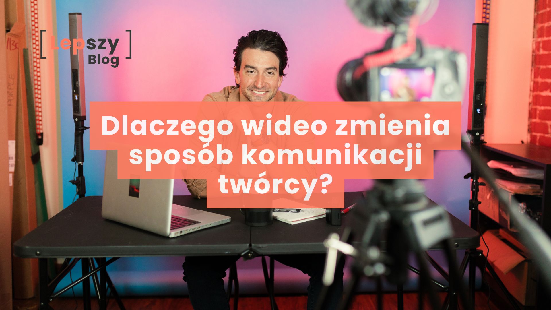 Rozmyty aparat na pierwszym planie i stojący w tle mężczyzna siedzący przy stole z tabletem oraz mikrofonem. Kolorowe, rozświetlone tło. Na środku nałożony tytuł: Dlaczego wideo zmienia sposób komunikacji twórcy?